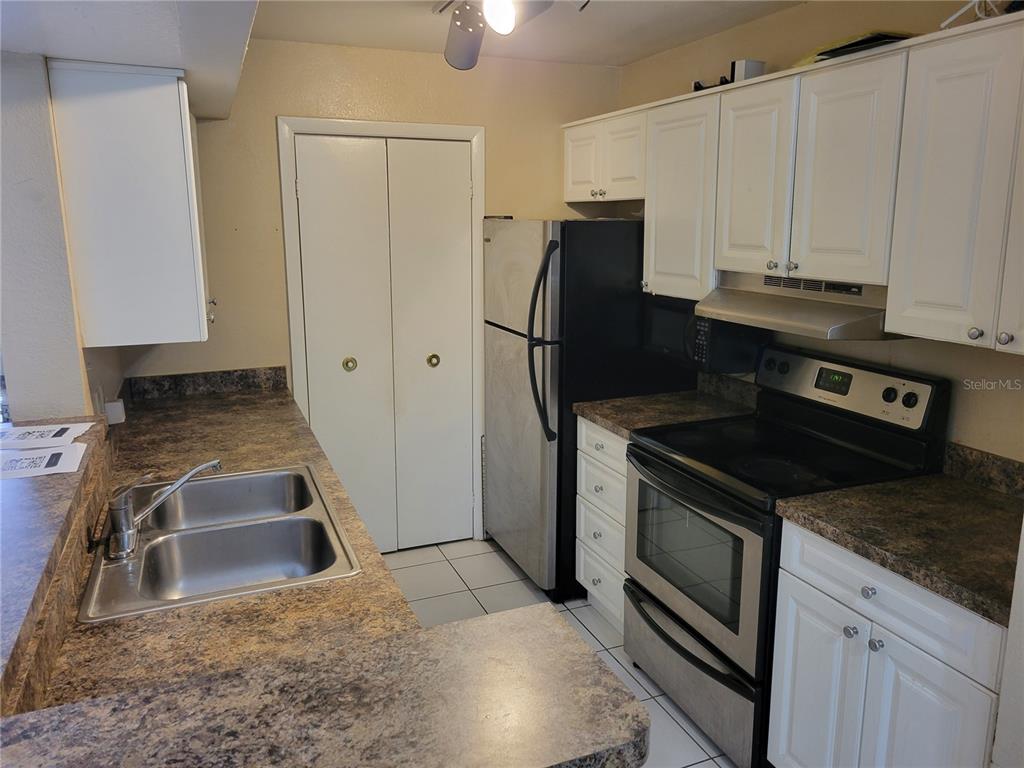 A kitchen features white cabinets, stainless steel appliances, a double sink, and dark laminate countertops — 5635 DEVONBRIAR WAY UNIT K204, ORLANDO, FL