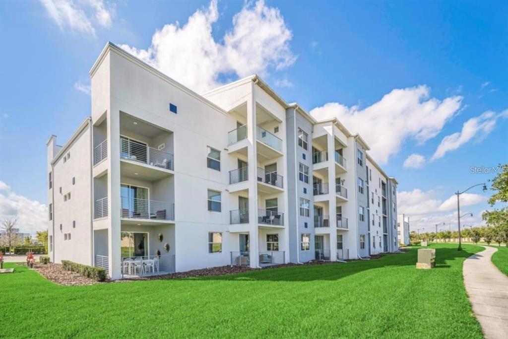 A multi-story apartment building with white stucco walls and private balconies under a blue sky — 4741 CLOCK TOWER DRIVE UNIT 208, KISSIMMEE, FL
