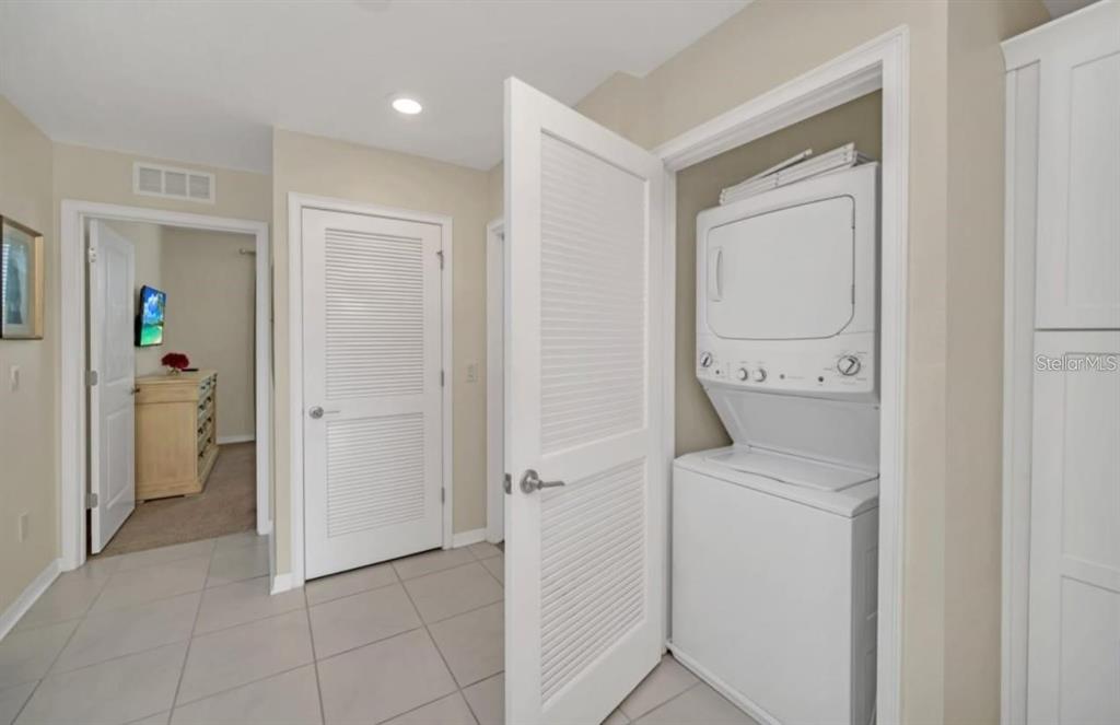 A laundry closet with a stacked washer and dryer sits in a tiled hallway — 4741 CLOCK TOWER DRIVE UNIT 208, KISSIMMEE, FL