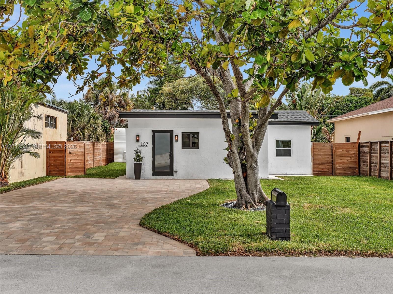 A white single-story house features a paved driveway, a large tree, and a wooden fence — 107 Central Ave, Delray Beach FL 33483, DELRAY BEACH, FL