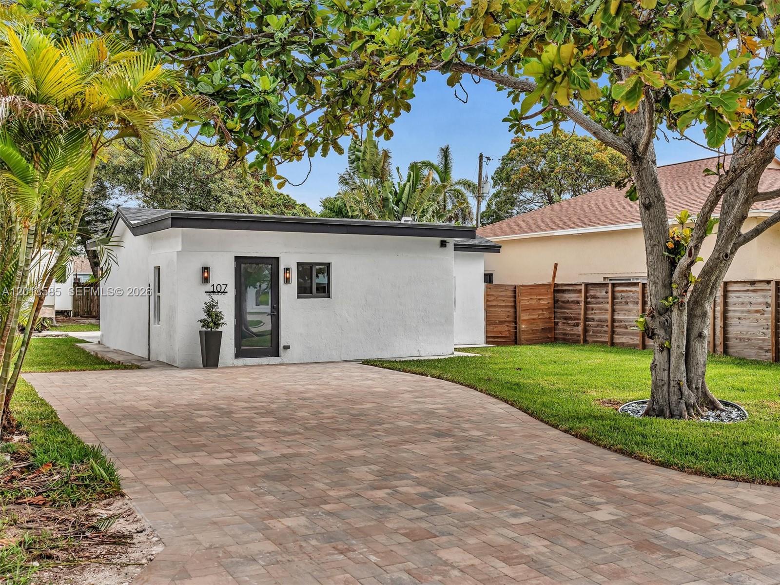 A small white house with a paved driveway and a wooden fence sits under trees — 107 Central Ave, Delray Beach FL 33483, DELRAY BEACH, FL