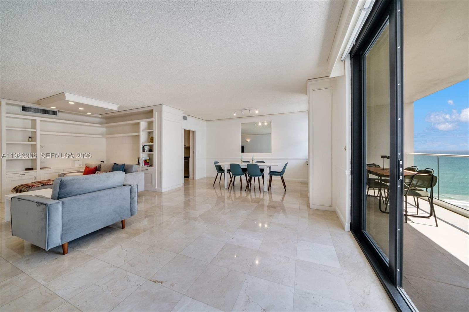 An open-concept living and dining area features marble floors, built-in shelving, and a balcony view — 9801 Collins Ave # 19H, Bal Harbour FL 33154, BAL HARBOUR, FL