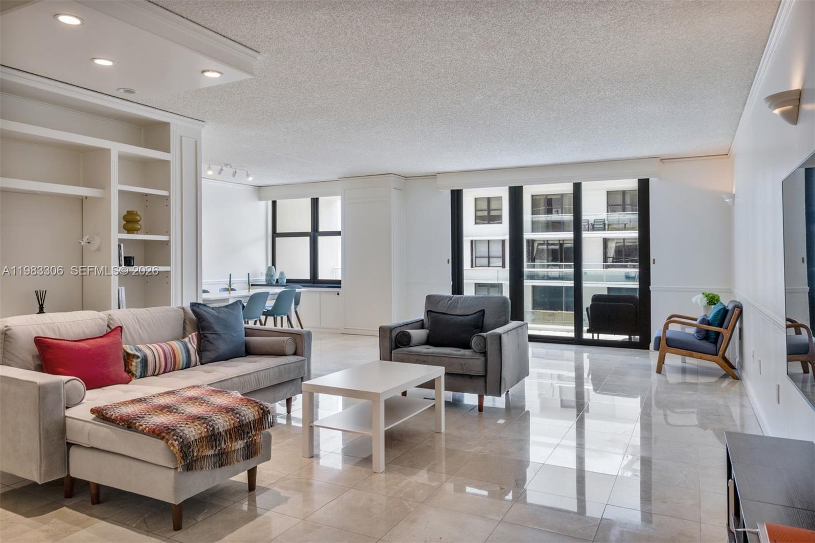 A bright living room features a grey sectional sofa, marble floors, and large glass balcony doors — 9801 Collins Ave # 19H, Bal Harbour FL 33154, BAL HARBOUR, FL