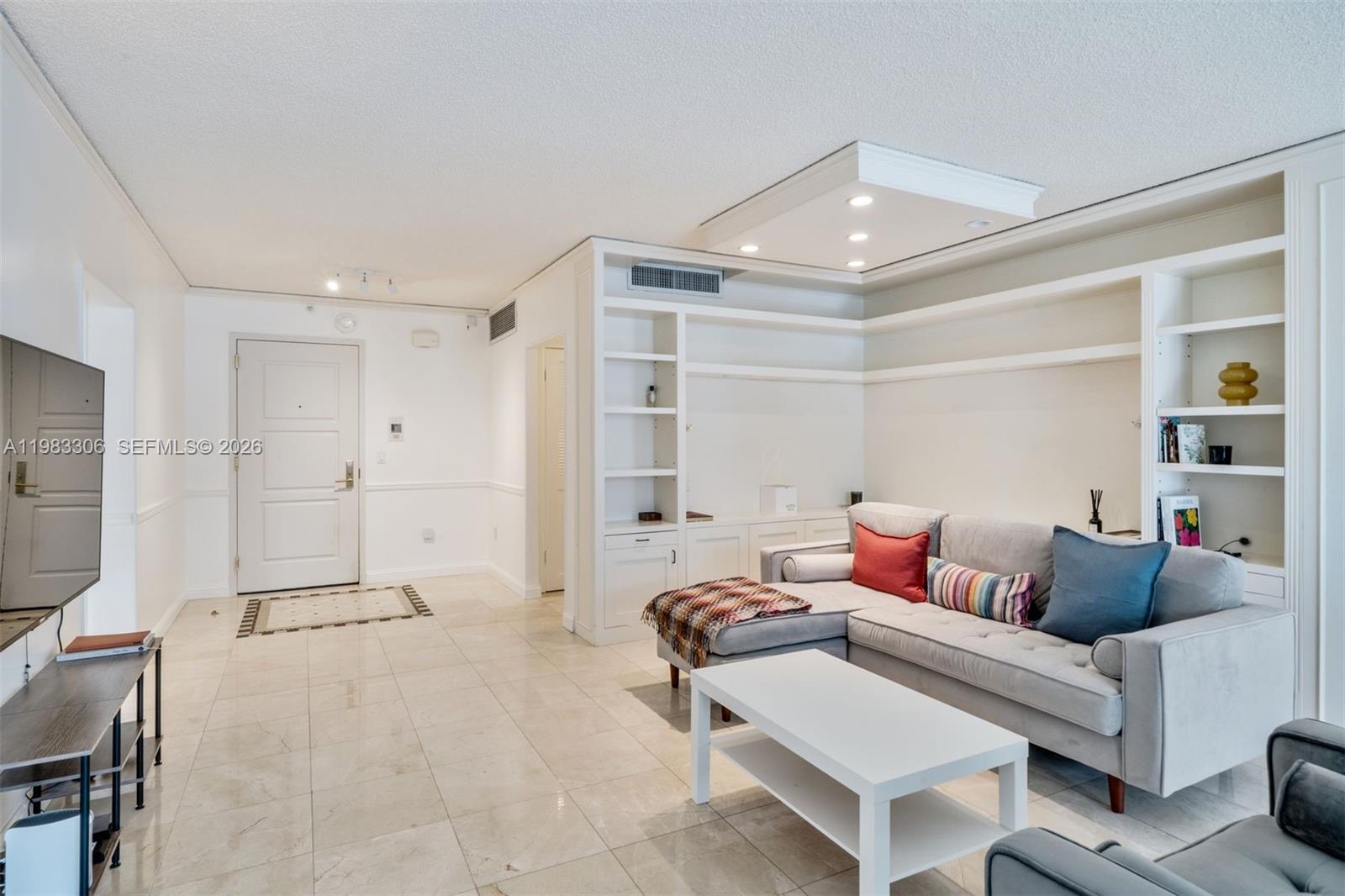 A living room features light tile floors, a grey sectional sofa, and built-in white shelving — 9801 Collins Ave # 19H, Bal Harbour FL 33154, BAL HARBOUR, FL