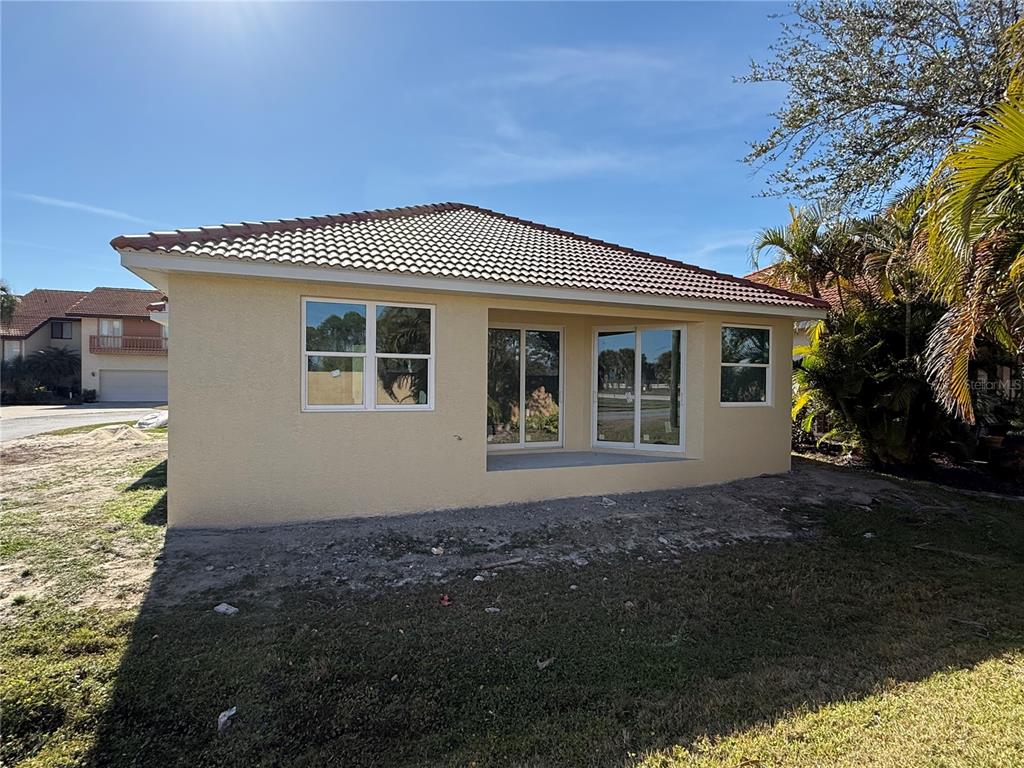 The exterior rear view of a tan house features a tiled roof and sliding glass doors — 0 SORRENTO PLACE, NOKOMIS, FL
