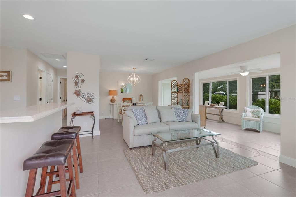 An open-concept living and dining area features tile flooring, a sofa, and bar seating — 320 GULF BOULEVARD UNIT 1A, BOCA GRANDE, FL