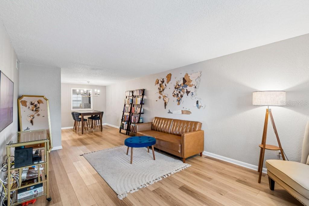 A living room features a brown leather sofa, blue ottoman, wall-mounted television, and wood flooring — 2500 LEE ROAD UNIT 104, WINTER PARK, FL