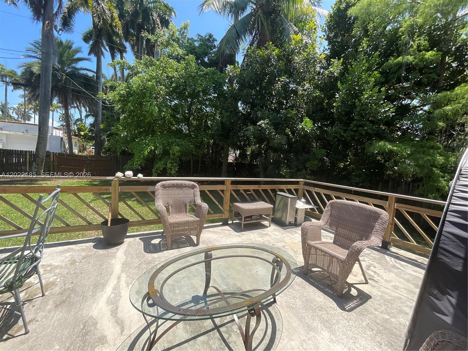A concrete patio features wicker chairs, a glass-topped table, and a wooden railing — 1206 Tyler St, Hollywood FL 33019, HOLLYWOOD, FL