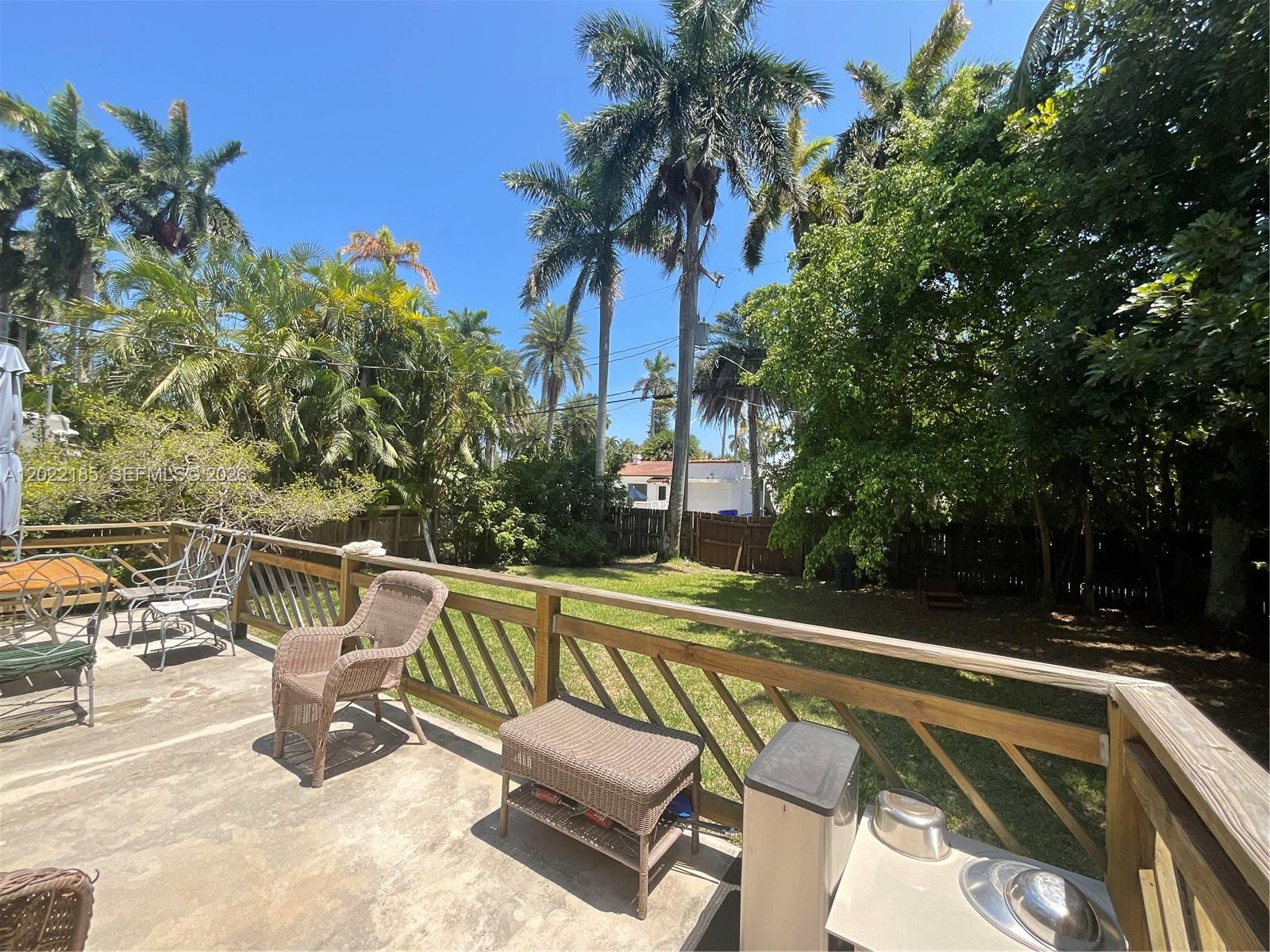 A wooden deck overlooks a grassy backyard filled with palm trees and lush foliage — 1206 Tyler St, Hollywood FL 33019, HOLLYWOOD, FL