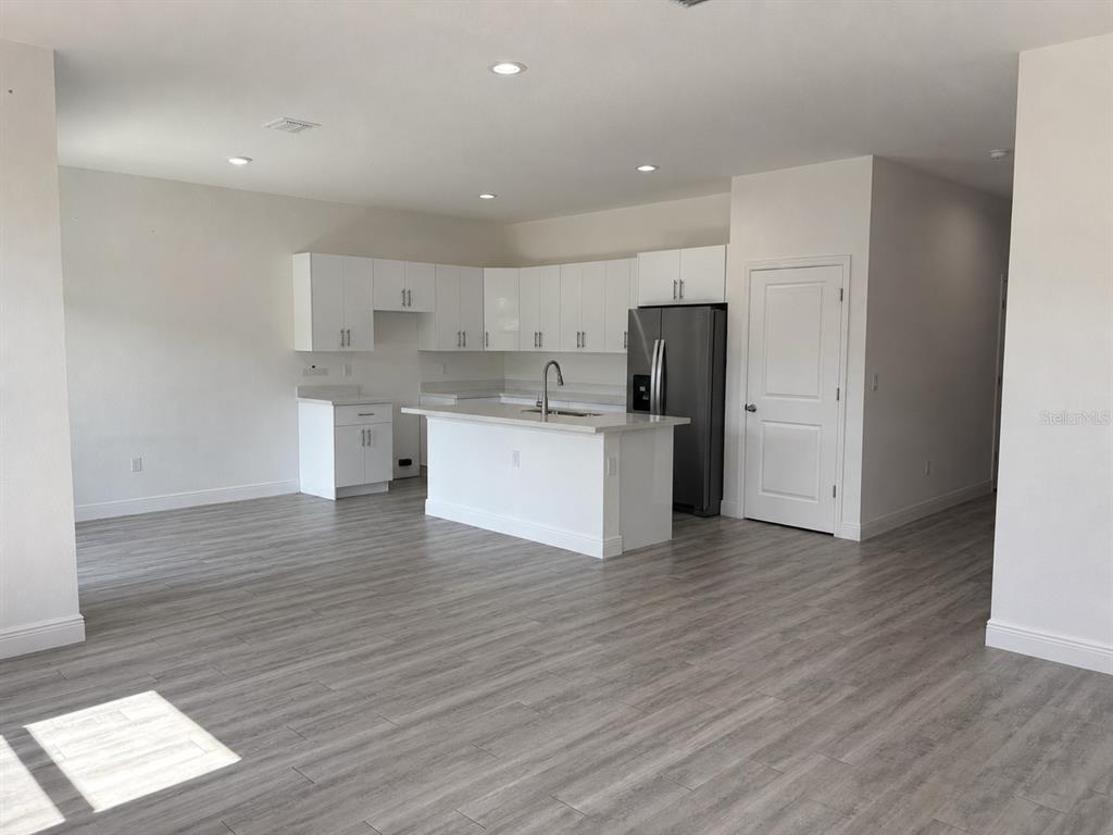 A modern kitchen features white cabinets, a central island with a sink, and light flooring — 3117 MEMPHIS LANE, LABELLE, FL