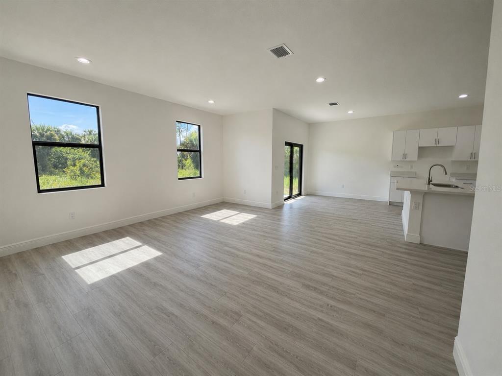 An open-concept living area features light wood-look flooring, white walls, and a kitchen with white cabinets — 3117 MEMPHIS LANE, LABELLE, FL