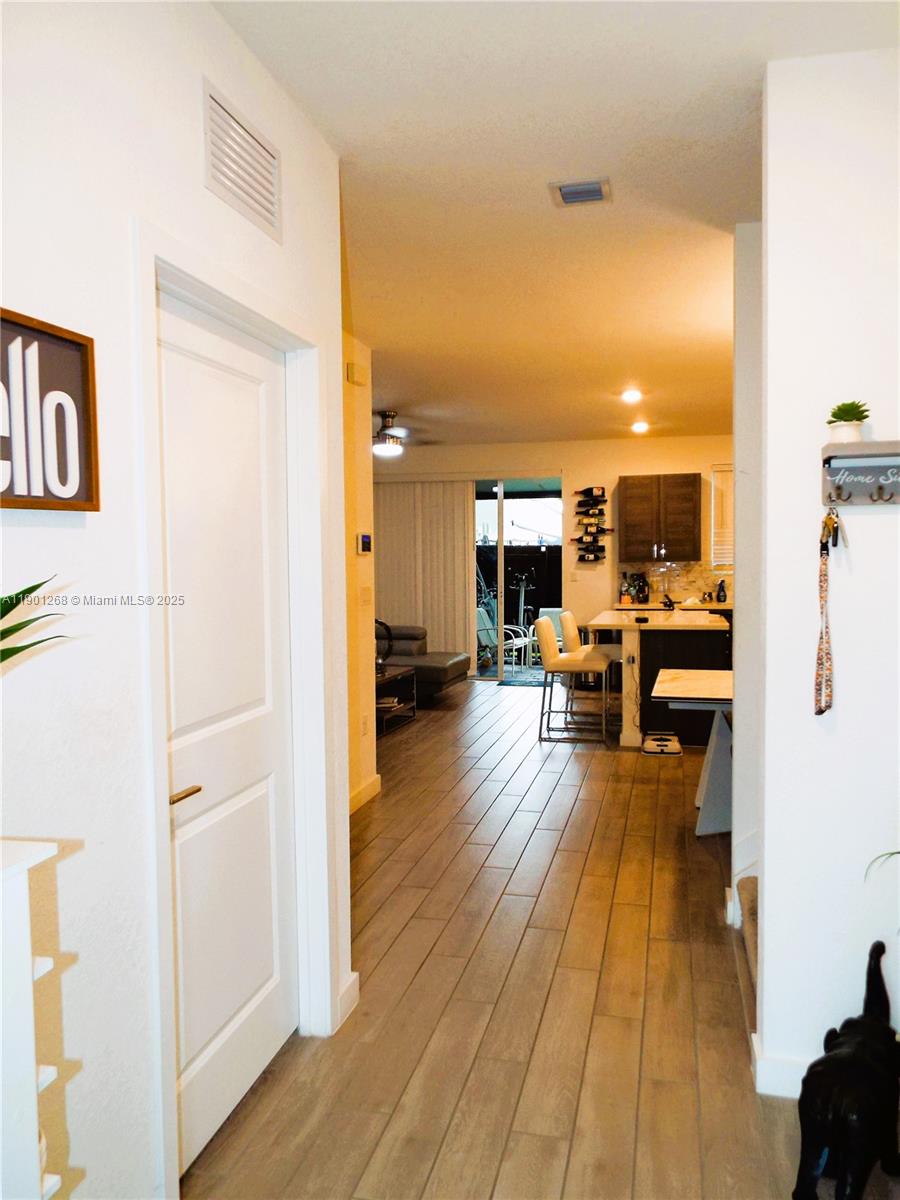 A hallway with wood-look tile flooring leads to an open-concept kitchen and living area — 2363 SE 11th St, Homestead FL 33035, HOMESTEAD, FL