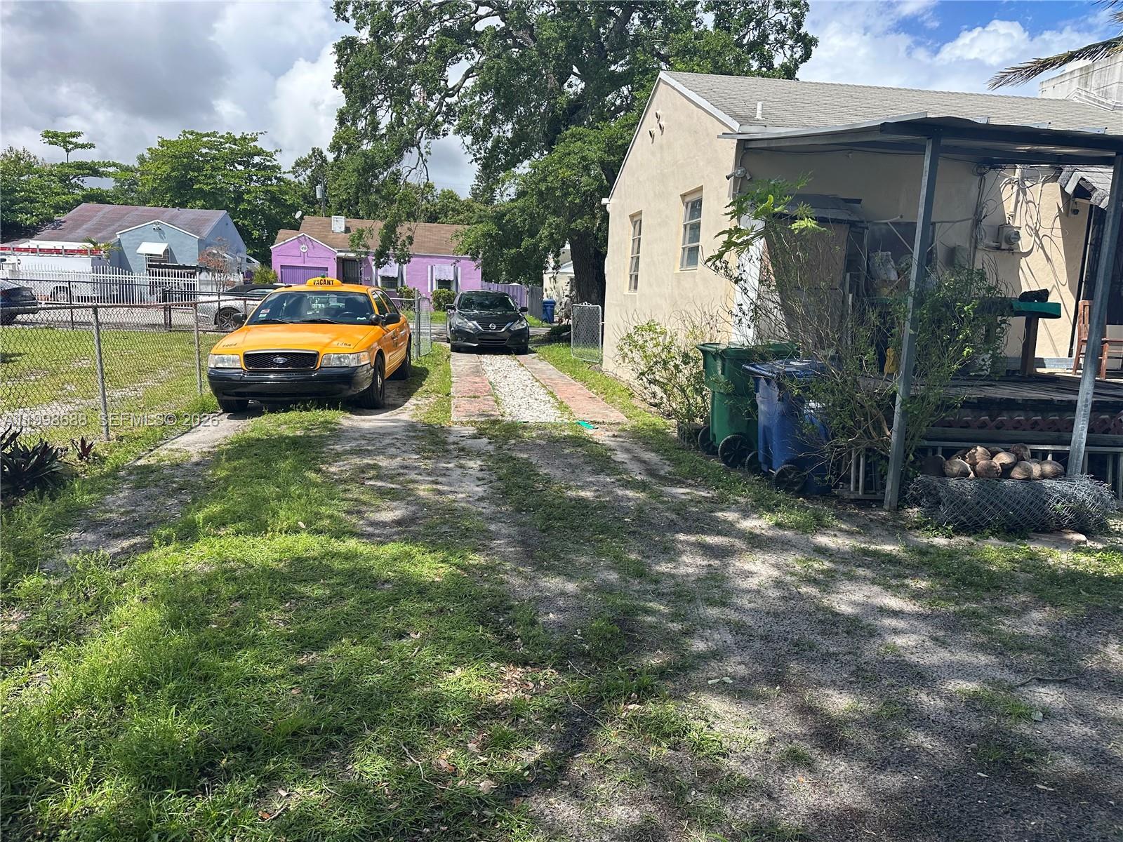 A yellow taxi and a black car are parked on a gravel driveway beside a house — 900 NW 75th St, Miami FL 33150, MIAMI, FL