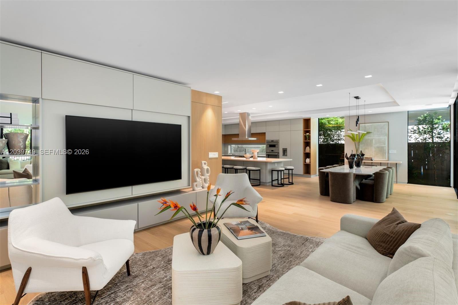 A modern open-concept living room features a large television, light wood flooring, and a kitchen — 3579 Avocado Ave, Miami FL 33133, MIAMI, FL
