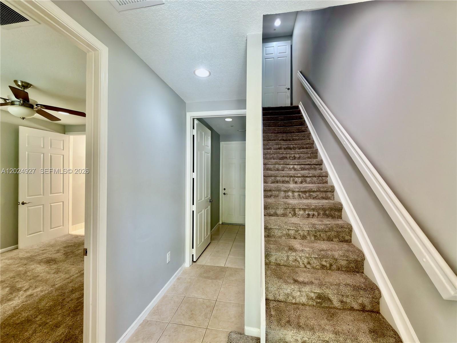 An interior view shows a carpeted staircase, a tiled hallway, and doorways to other rooms — 3909 White Peacock Ln, Coconut Creek FL 33073, COCONUT CREEK, FL