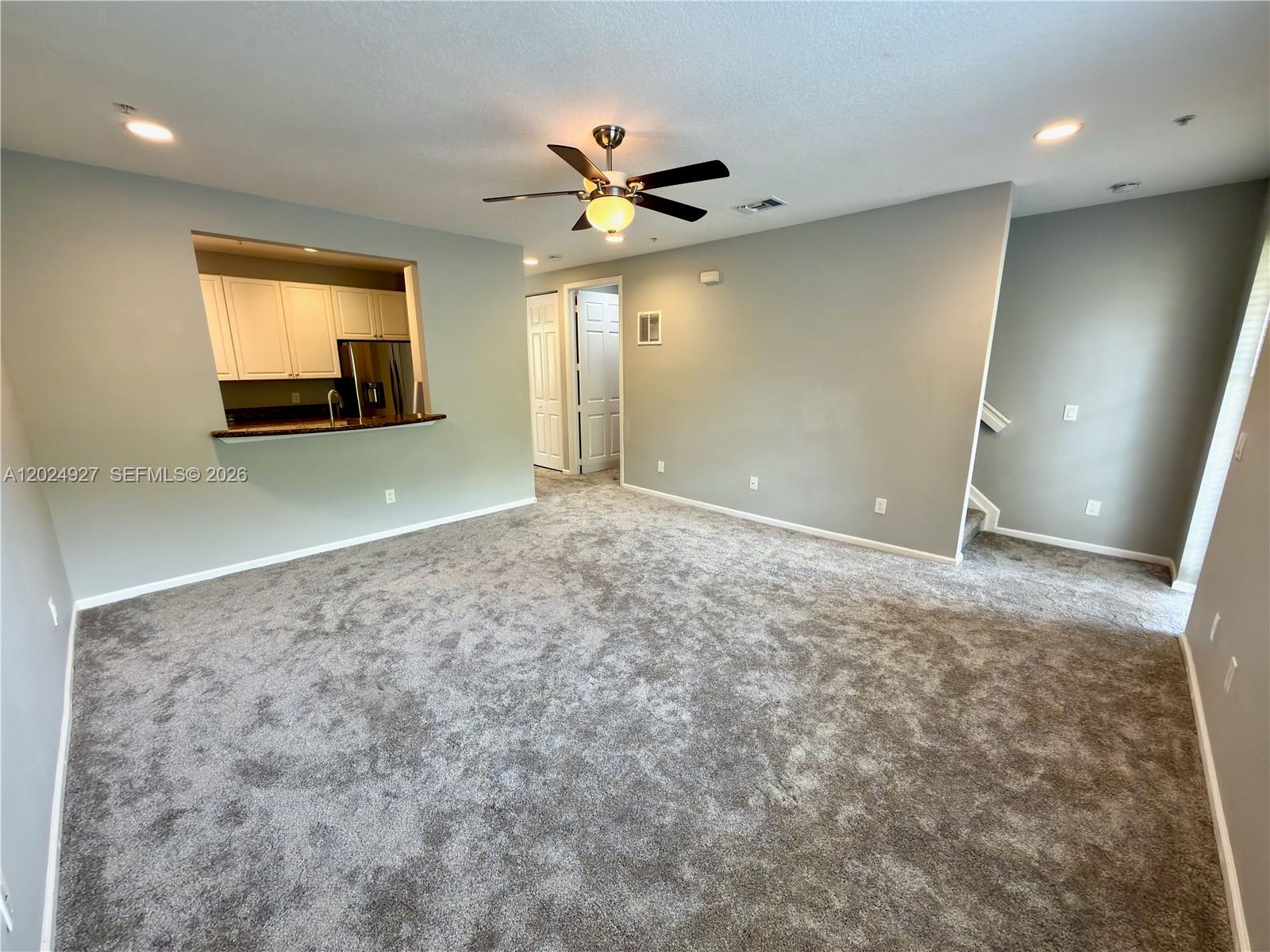 A living room features gray carpeting, light gray walls, a ceiling fan, and a kitchen pass-through — 3909 White Peacock Ln, Coconut Creek FL 33073, COCONUT CREEK, FL