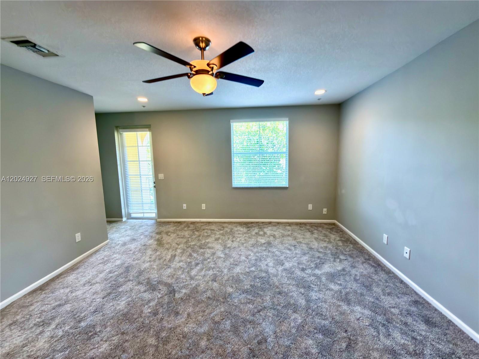 An empty room features gray walls, gray carpeting, a ceiling fan, and a glass door — 3909 White Peacock Ln, Coconut Creek FL 33073, COCONUT CREEK, FL