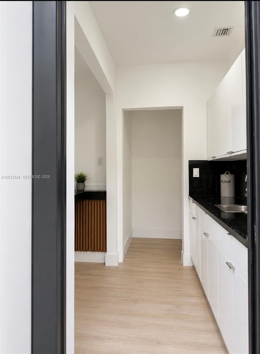 A narrow kitchen features white cabinets, black countertops, and light wood-look flooring — 23041 SW 107th Ave # 2, Miami FL 33170, MIAMI, FL