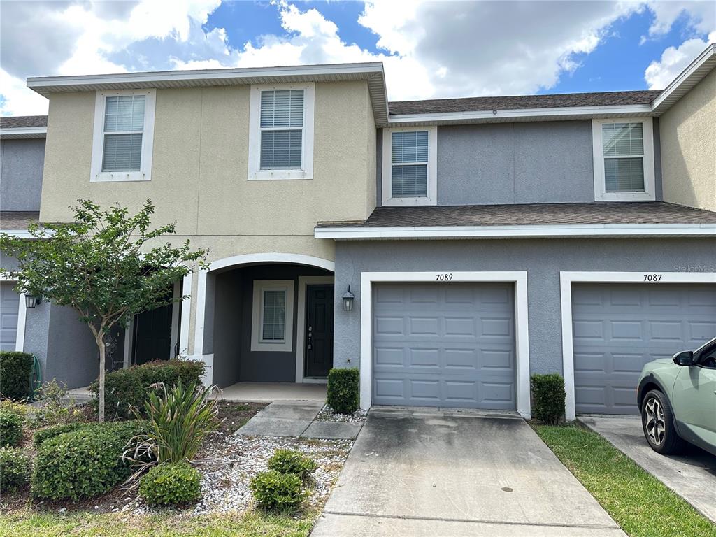 A two-story townhouse exterior features a gray garage, beige and gray stucco, and a driveway — 7089 WOODCHASE GLEN DRIVE, RIVERVIEW, FL