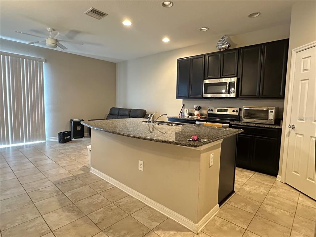 A kitchen features a granite-topped island, dark cabinetry, and tile flooring in an open-concept space — 7089 WOODCHASE GLEN DRIVE, RIVERVIEW, FL