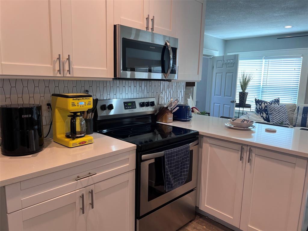 A kitchen features white cabinets, a stainless steel stove, a microwave, and a yellow coffee maker — 1137 HIGHLAND STREET S, ST PETERSBURG, FL