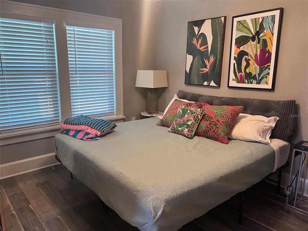 A bedroom features a bed with a gray headboard, tropical wall art, and wood flooring — 1137 HIGHLAND STREET S, ST PETERSBURG, FL