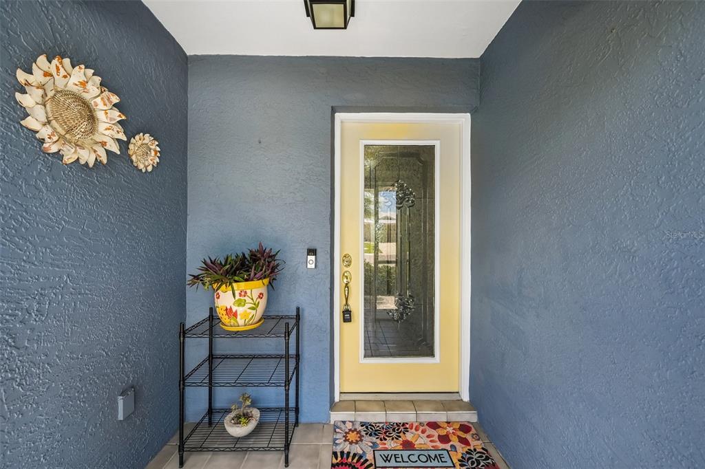 A front entryway features a yellow door, blue walls, a metal shelf, and a welcome mat — 2025 NEW BEDFORD DRIVE, SUN CITY CENTER, FL