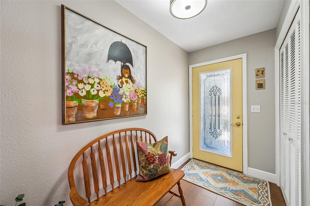 A wooden bench sits beneath a painting in an entryway with a yellow front door — 2025 NEW BEDFORD DRIVE, SUN CITY CENTER, FL