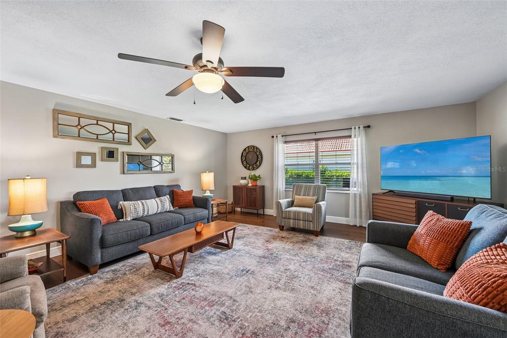 A living room features two gray sofas, a patterned area rug, and a ceiling fan — 2025 NEW BEDFORD DRIVE, SUN CITY CENTER, FL