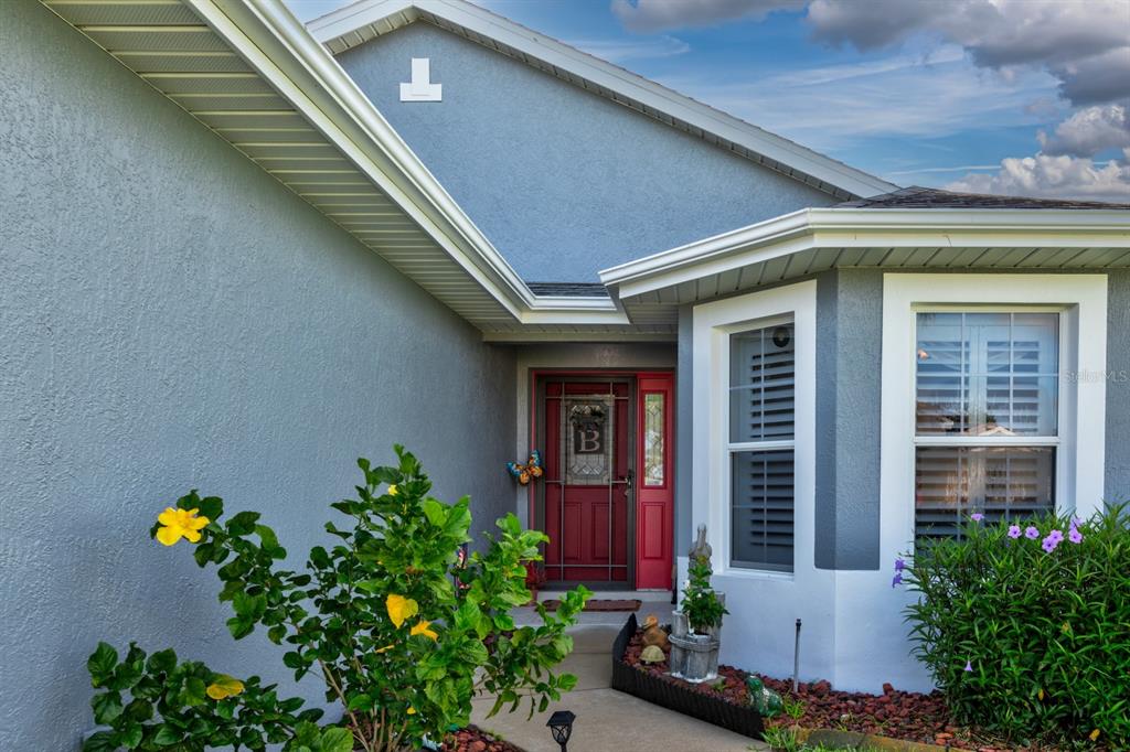A blue house exterior features a red front door, a bay window, and landscaping — 27336 PINE STRAW ROAD, LEESBURG, FL