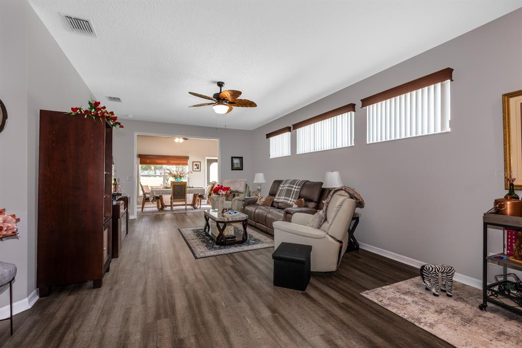A living room with wood-look flooring, a ceiling fan, and a view into a dining area — 27336 PINE STRAW ROAD, LEESBURG, FL