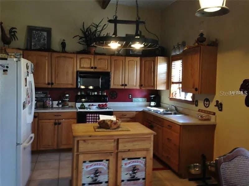 A kitchen features wood cabinets, a central island, and a wagon wheel chandelier — 54523 ASTOR TRANSFER STATION ROAD, ASTOR, FL