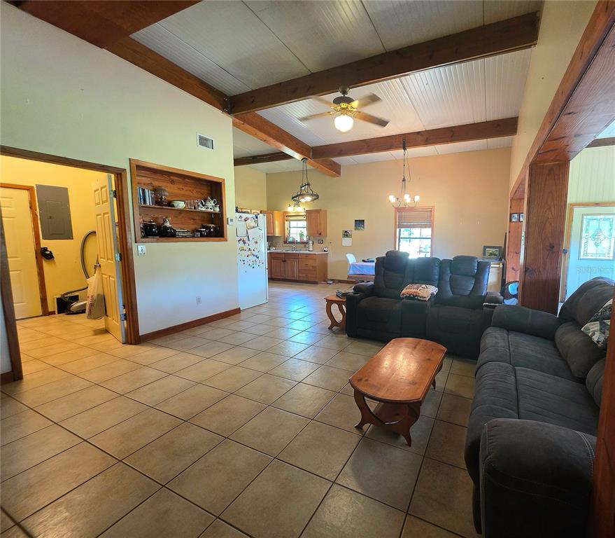 A living room with tile floors and exposed wood beams opens into a kitchen area — 54523 ASTOR TRANSFER STATION ROAD, ASTOR, FL