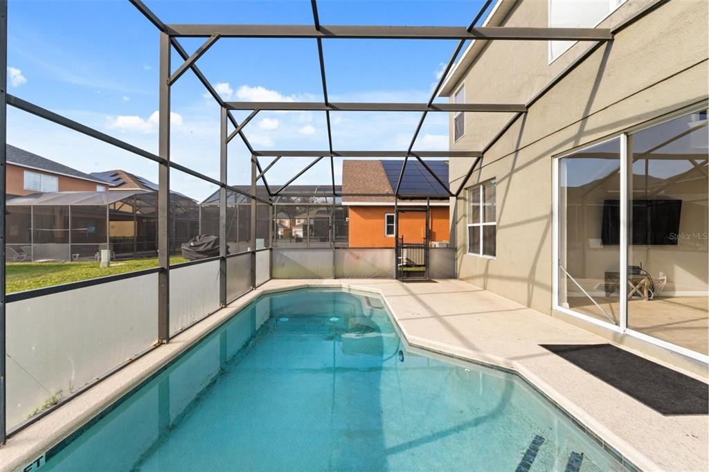 A swimming pool with a screened-in lanai sits behind a two-story stucco house — 158 BAREFOOT BEACH WAY, KISSIMMEE, FL
