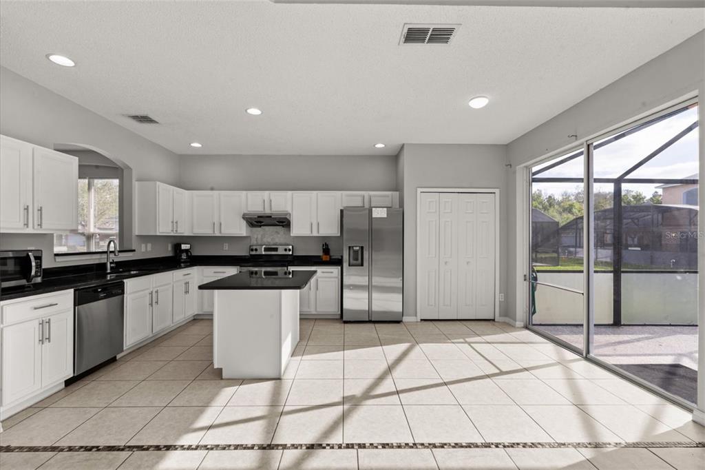 A kitchen with white cabinets, black countertops, a center island, and sliding glass patio doors — 158 BAREFOOT BEACH WAY, KISSIMMEE, FL