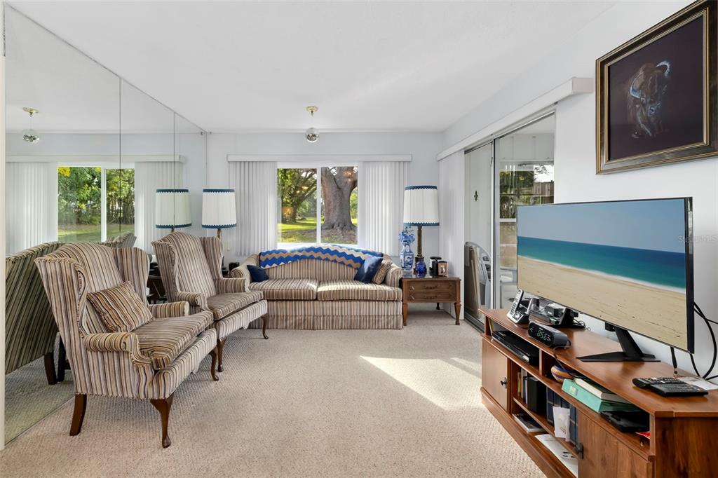 A living room features striped furniture, a large mirror wall, and a television on a stand — 4586 MOHICAN TRAIL UNIT 147, SARASOTA, FL