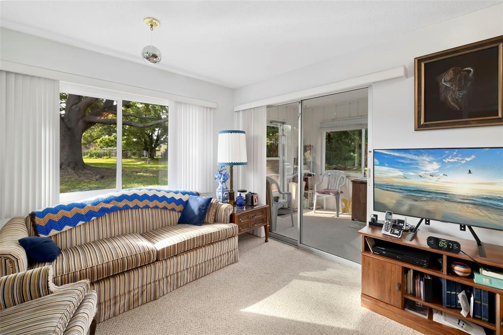 A living room features a striped sofa, a television on a wooden stand, and sliding doors — 4586 MOHICAN TRAIL UNIT 147, SARASOTA, FL