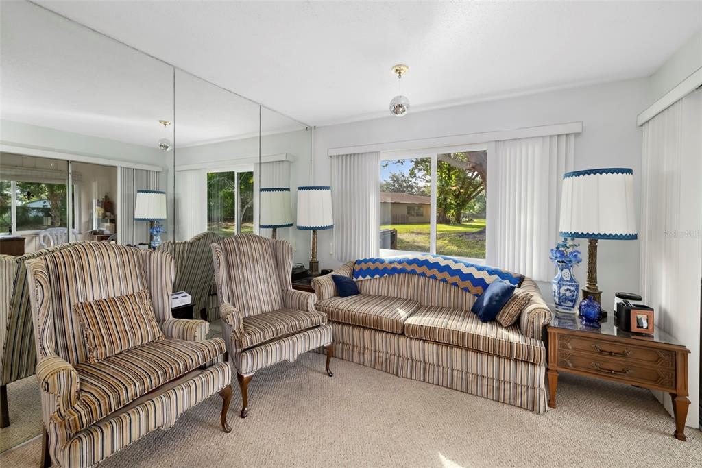 A living room features striped furniture, a mirrored wall, and a large window overlooking trees — 4586 MOHICAN TRAIL UNIT 147, SARASOTA, FL