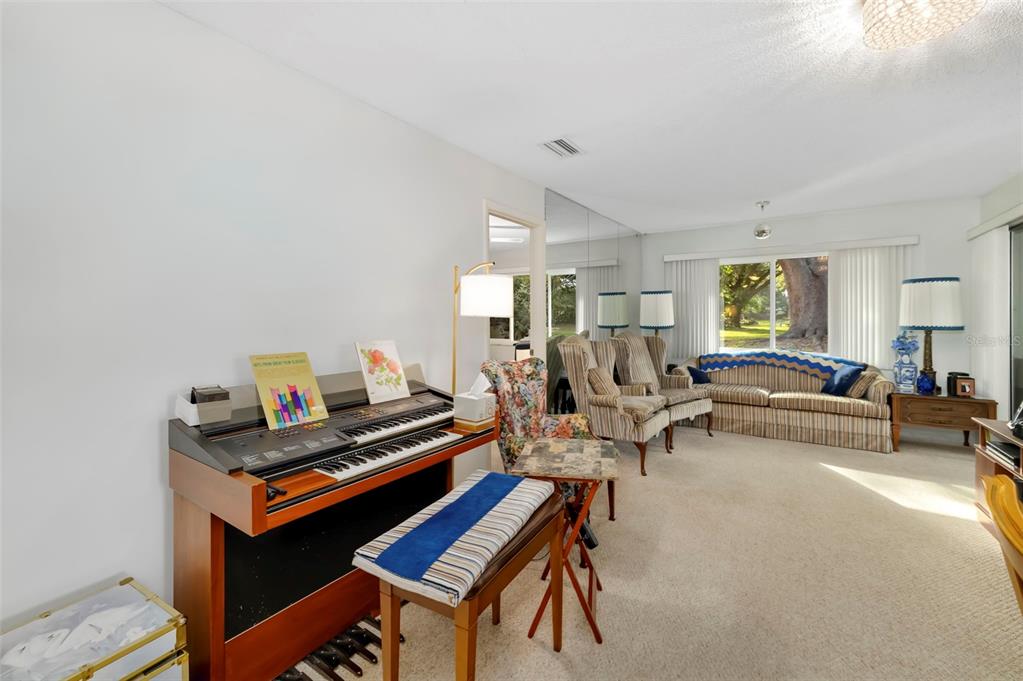 A living room features a wooden electronic organ, patterned armchairs, a striped sofa, and carpeting — 4586 MOHICAN TRAIL UNIT 147, SARASOTA, FL