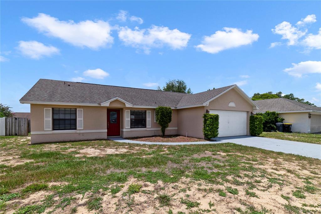 A single-story house with a tan exterior, a red front door, and a two-car garage — 127 CITRUSWOOD COURT, DAVENPORT, FL