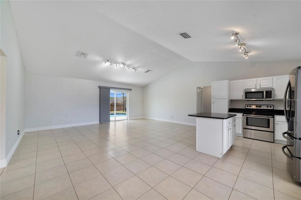 An open-concept kitchen and living area with white cabinets, stainless appliances, and tile flooring — 127 CITRUSWOOD COURT, DAVENPORT, FL