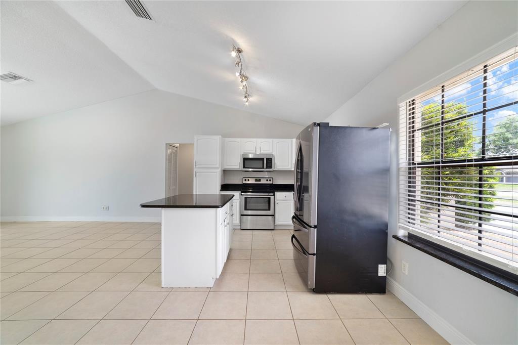 A kitchen with white cabinets, stainless steel appliances, a dark island, and tile flooring — 127 CITRUSWOOD COURT, DAVENPORT, FL