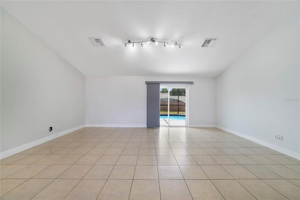 A spacious, empty room with light-colored tile flooring, white walls, and a sliding glass door — 127 CITRUSWOOD COURT, DAVENPORT, FL