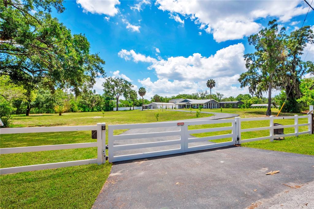 A white fence and gate open to a paved driveway leading to a house — 5785 GILLIAM ROAD, ORLANDO, FL