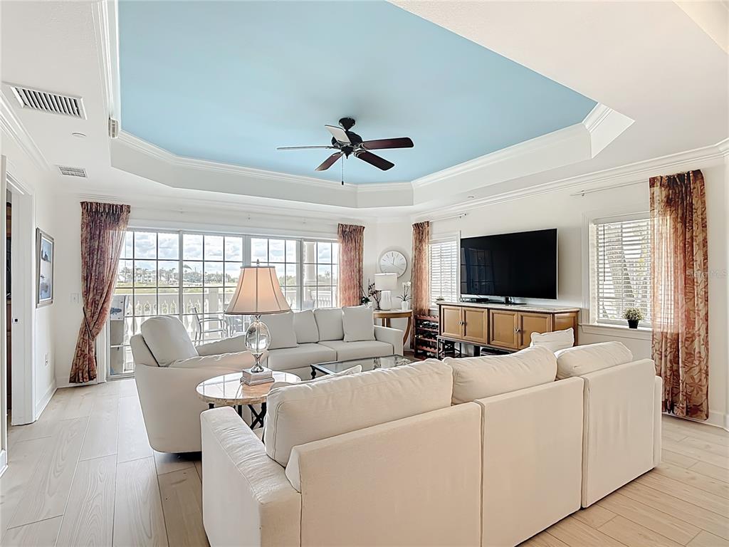 A living room features a blue tray ceiling, white sofas, and large windows with water views — 1362 CENTRE COURT RIDGE DRIVE UNIT 204, REUNION, FL