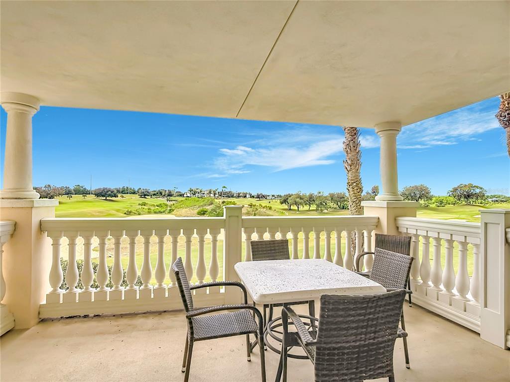 A covered balcony features a stone table, chairs, and a view of a golf course — 1362 CENTRE COURT RIDGE DRIVE UNIT 204, REUNION, FL