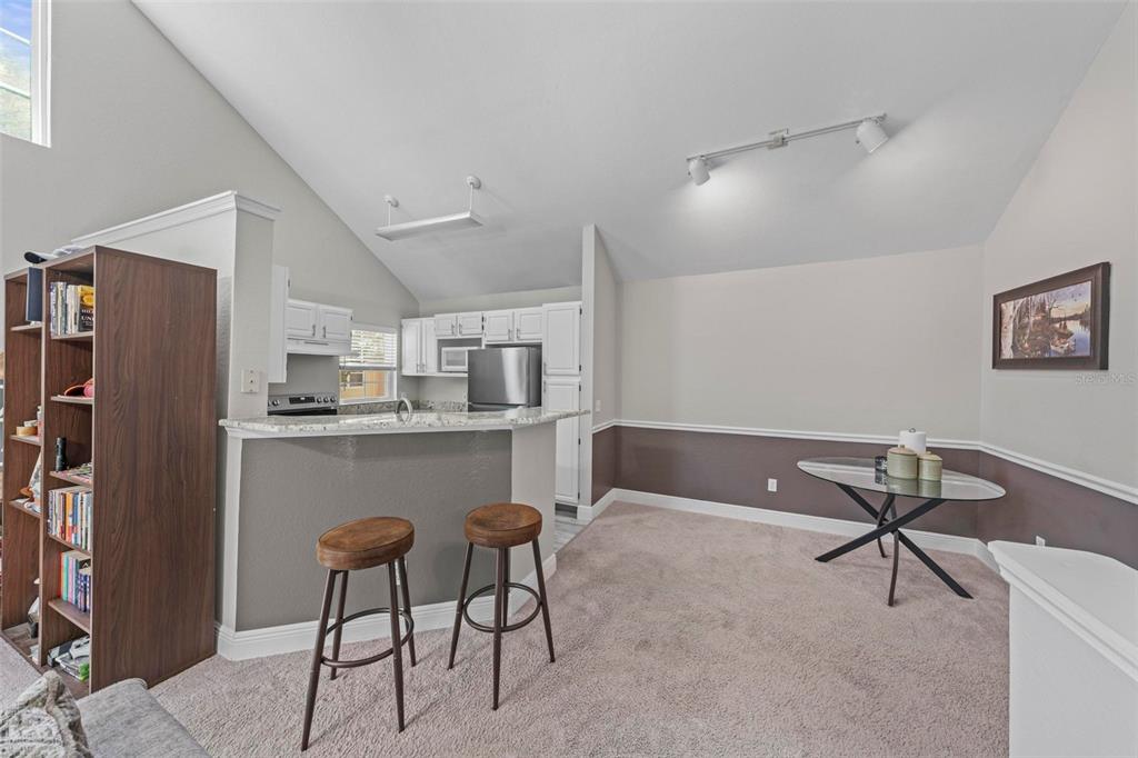A kitchen with a breakfast bar and dining area featuring carpeted floors and vaulted ceilings — 3396 PARKCHESTER SQUARE BOULEVARD UNIT 204, ORLANDO, FL