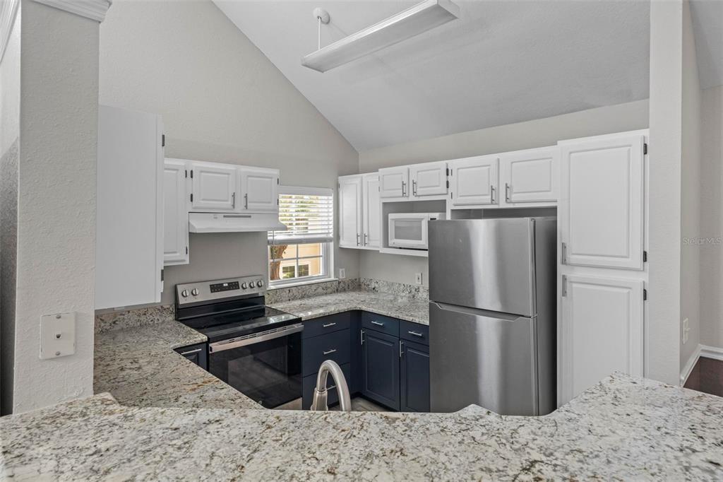 A kitchen features white upper cabinets, dark blue lower cabinets, granite countertops, and stainless appliances — 3396 PARKCHESTER SQUARE BOULEVARD UNIT 204, ORLANDO, FL