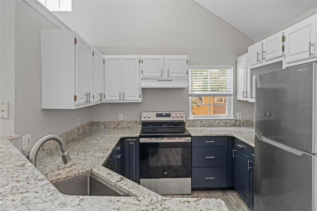 A kitchen features white upper cabinets, dark lower cabinets, granite countertops, and stainless steel appliances — 3396 PARKCHESTER SQUARE BOULEVARD UNIT 204, ORLANDO, FL