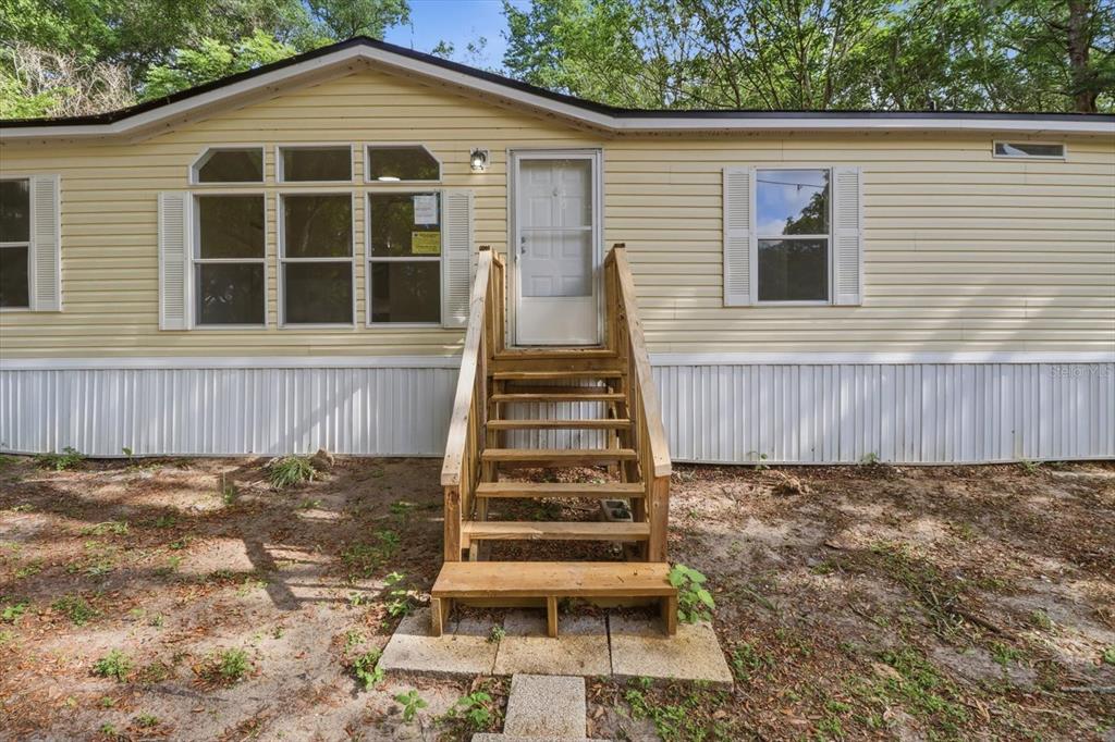 A yellow mobile home exterior features a wooden staircase leading to a white front door — 2565 E NORTH STREET, INVERNESS, FL